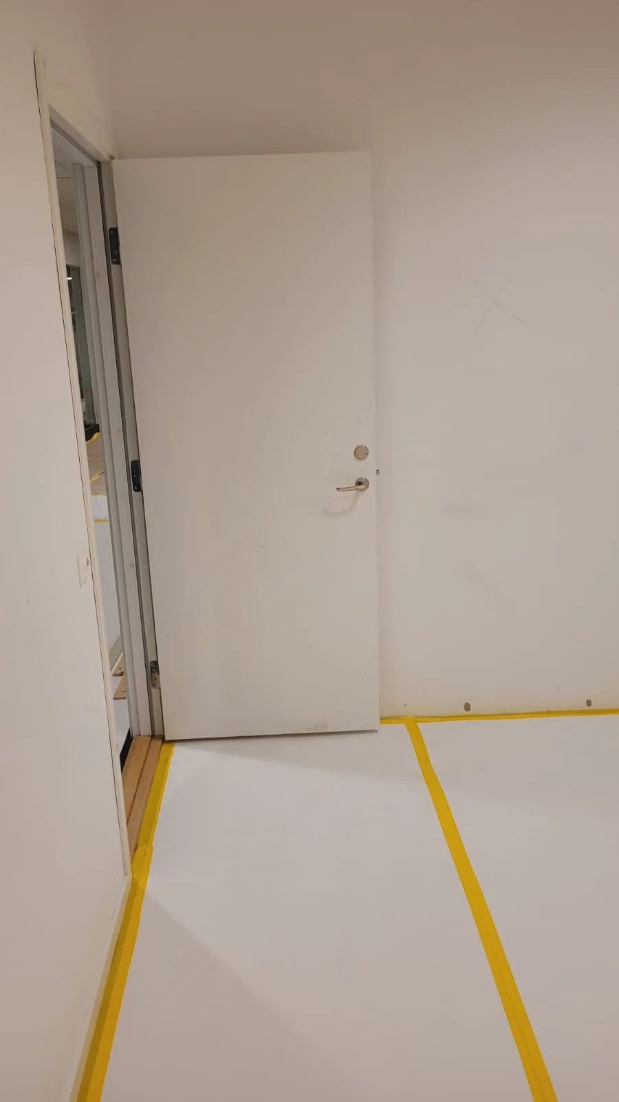 Renovering av rum med ny vit dörr och markerad golvlinje