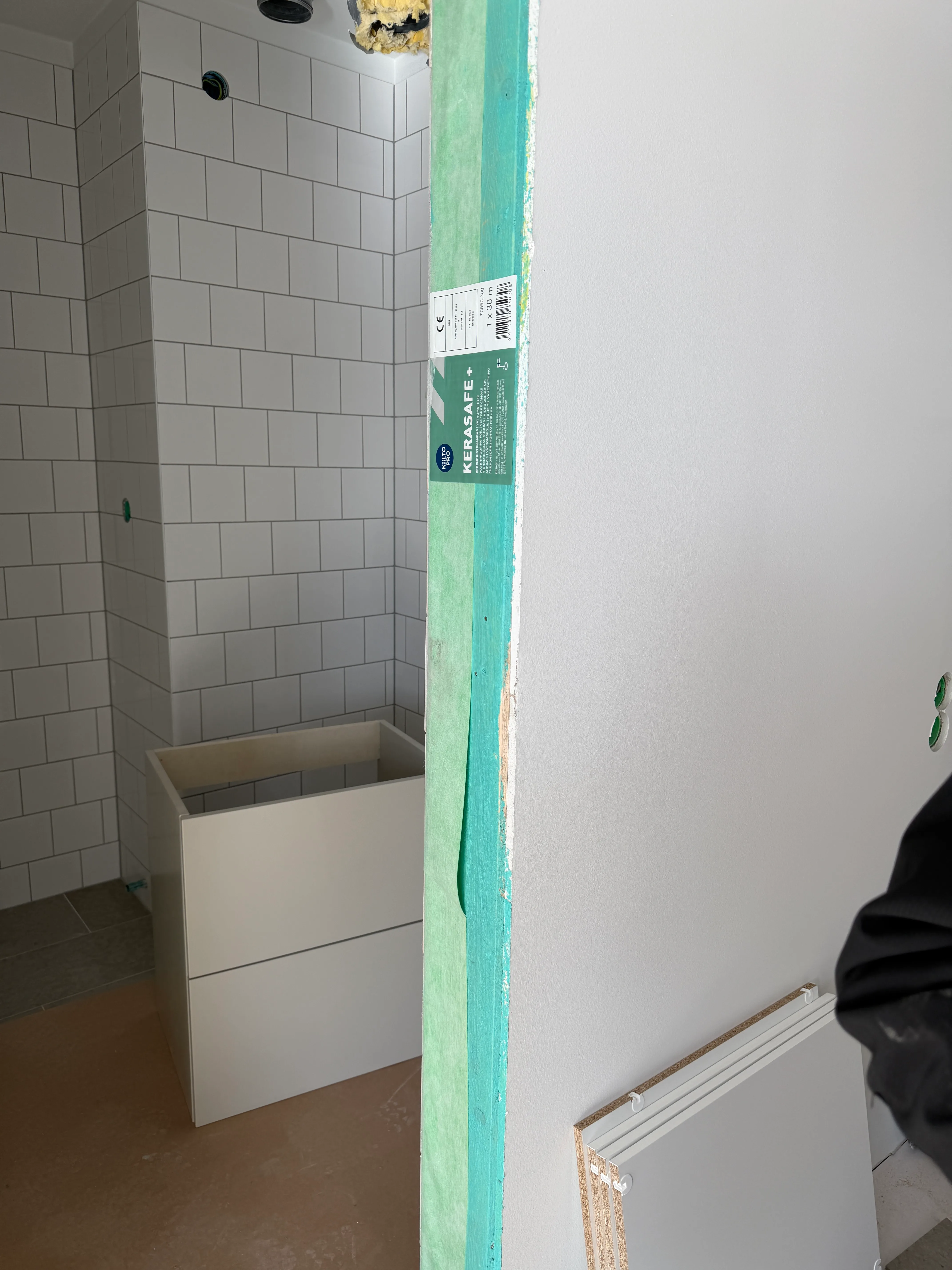 Del av ett badrum med vitkaklade väggar och en kommande duschavskiljare
