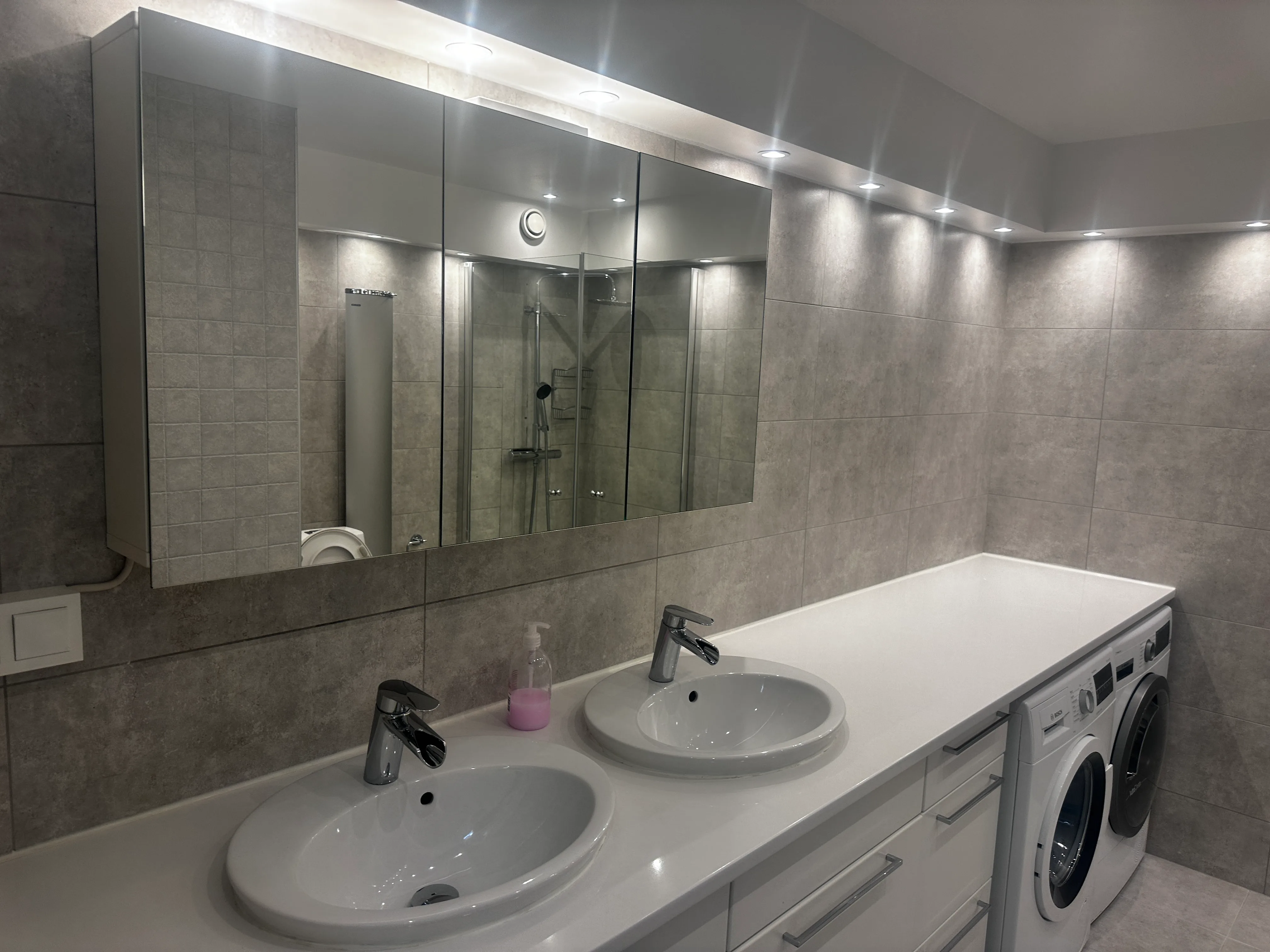 Modernt badrum med dubbelhandfat och tvättmaskin, belyst med LED-lampor