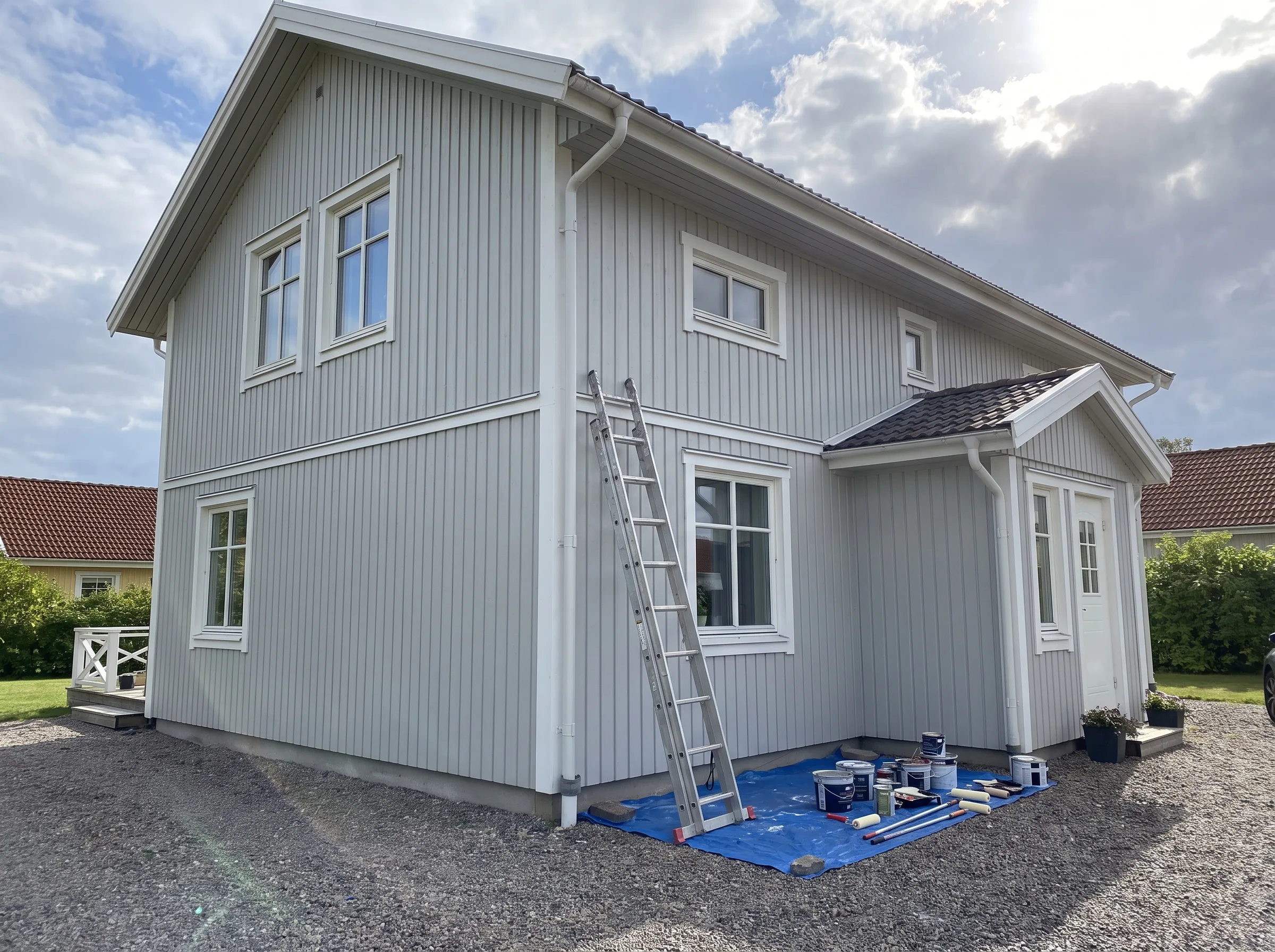 Husrenovering av ett grått hus med stege och färgmaterial synliga