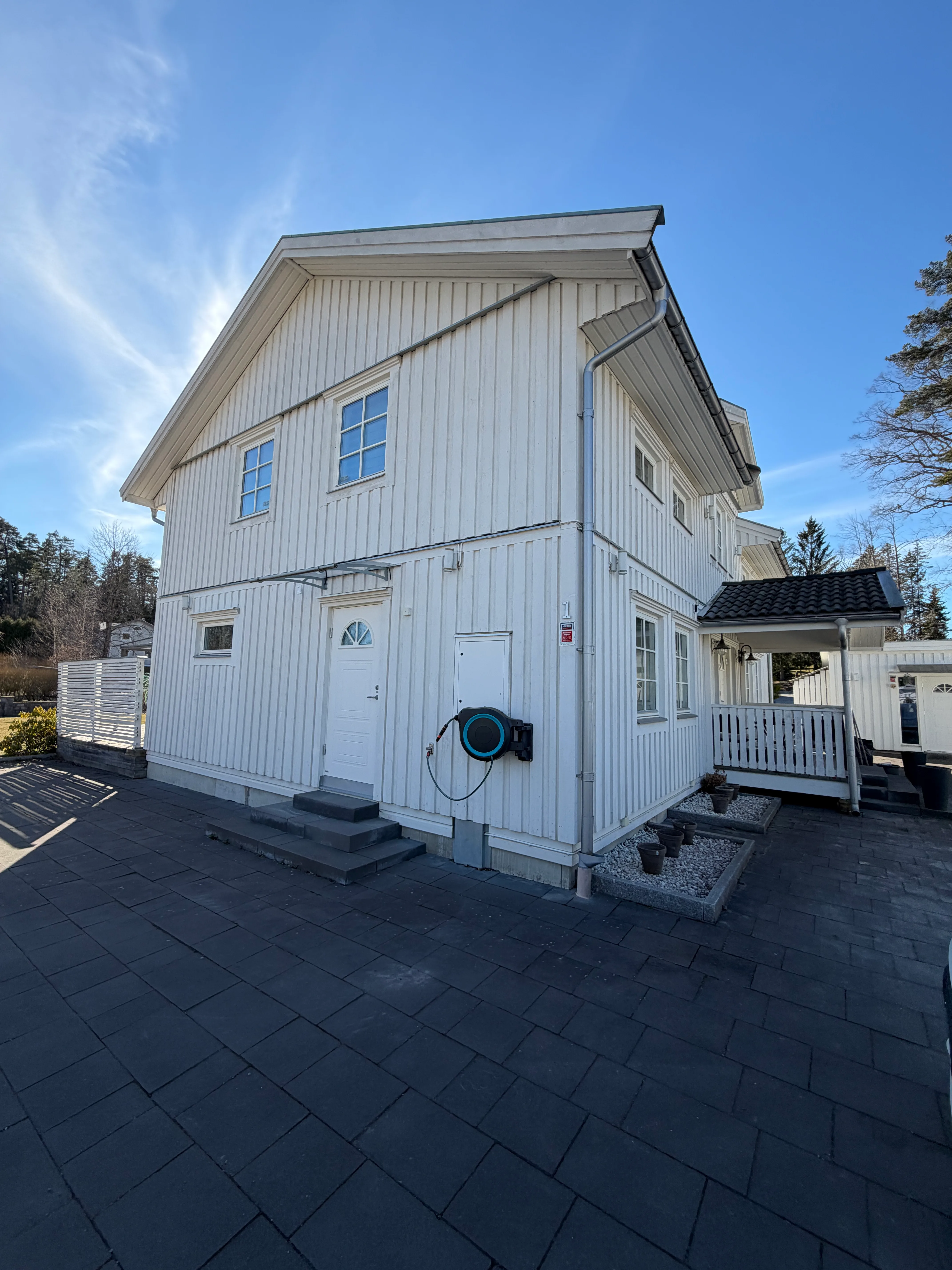 Nybyggnation av ett vitt hus med träfasad och gård i soligt väder