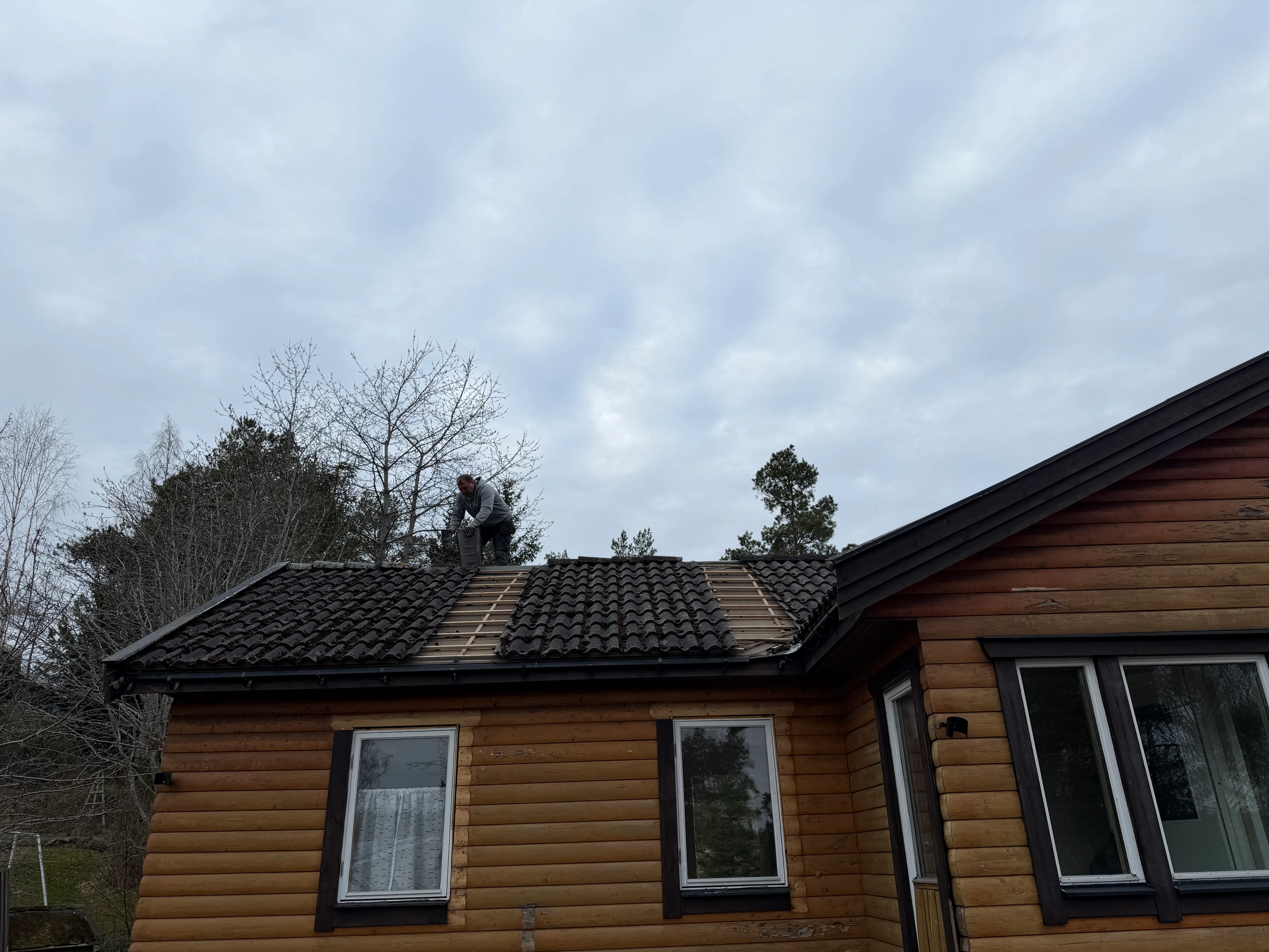 Takläggning av takpannor på en träbyggnad med grunt arbete i bakgrunden