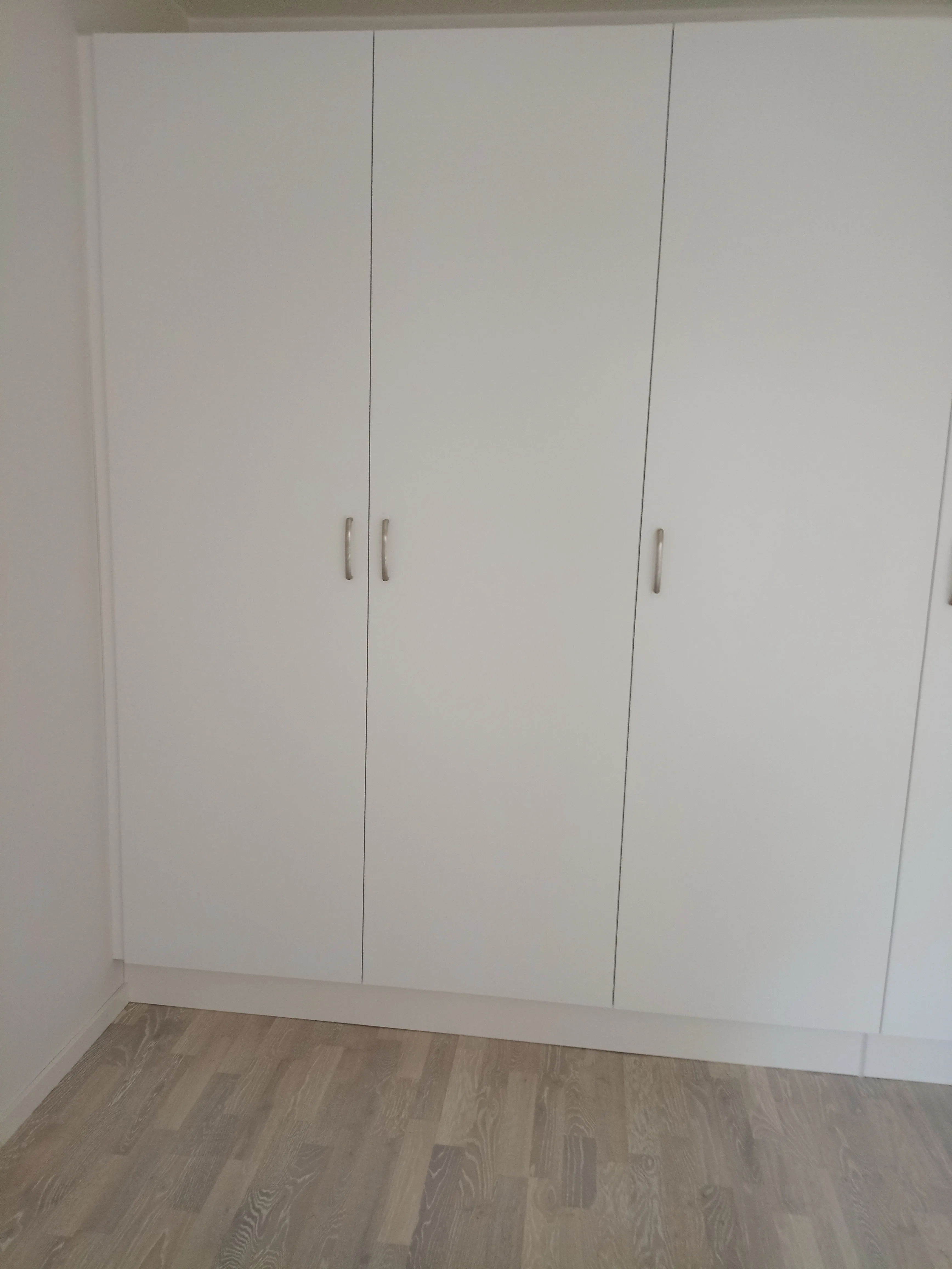 Nyinstallerad vit garderob med tre dörrar i rum med ljus trägolv